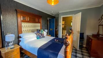 A hotel room with a large bed, a wooden headboard, a nightstand with a lamp, and a checkered floor.