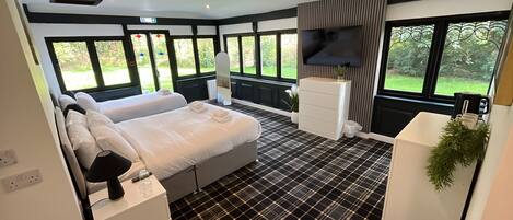 A hotel room with a bed, bedside table, TV, and large windows.