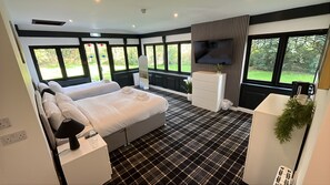 A hotel room with a bed, bedside table, TV, and large windows. - The Old Mill Inn  (Forres)