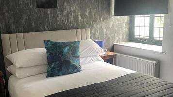 A neatly made bed with a headboard, a pillow, and a blanket. There is a window with a view of the outside.