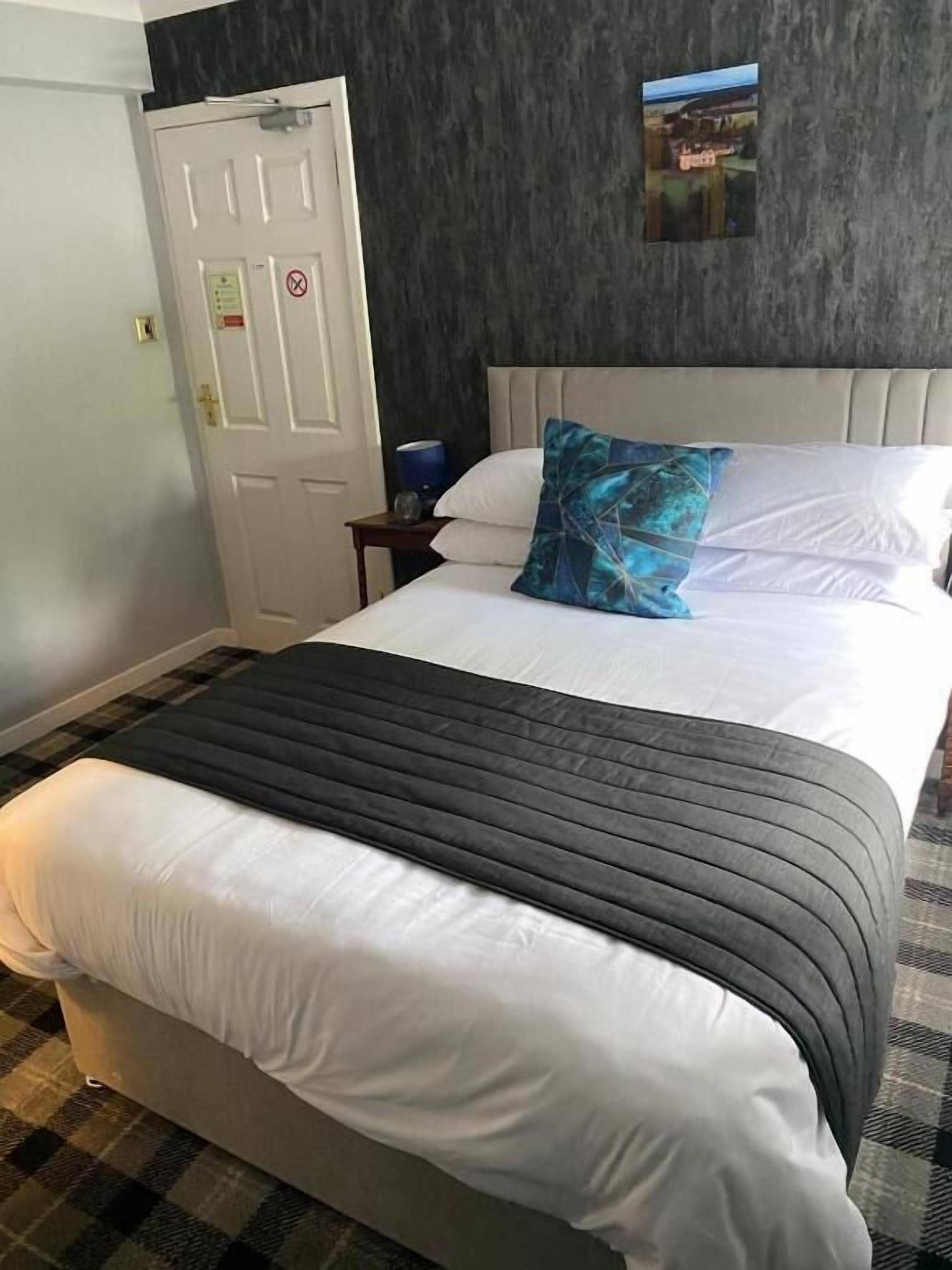 Una habitación de hotel con cama, mesita de noche, una puerta y un cuadro colgado en la pared.