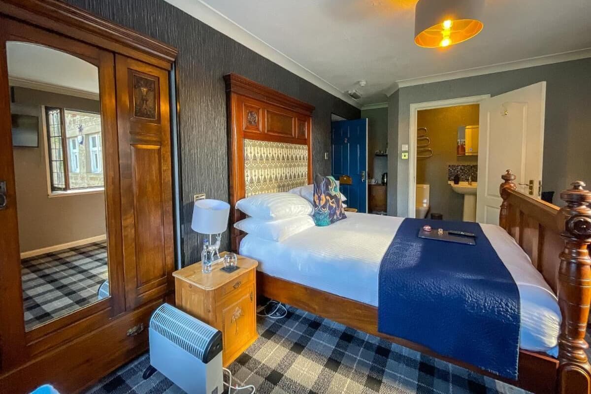 A hotel room with a large bed, a wooden wardrobe, a bedside table with a lamp, and a checkered floor.