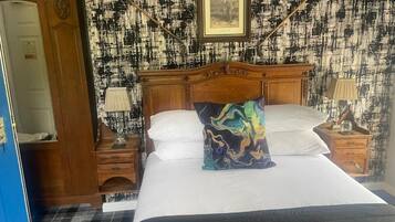 A hotel room with a bed, a wooden wardrobe, a nightstand with a lamp, and a wall with a framed picture.