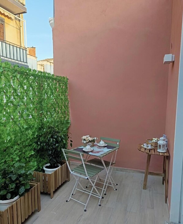 En lille patio med et bord og stole, en grøn plantevæg og en lille hylde med ting.