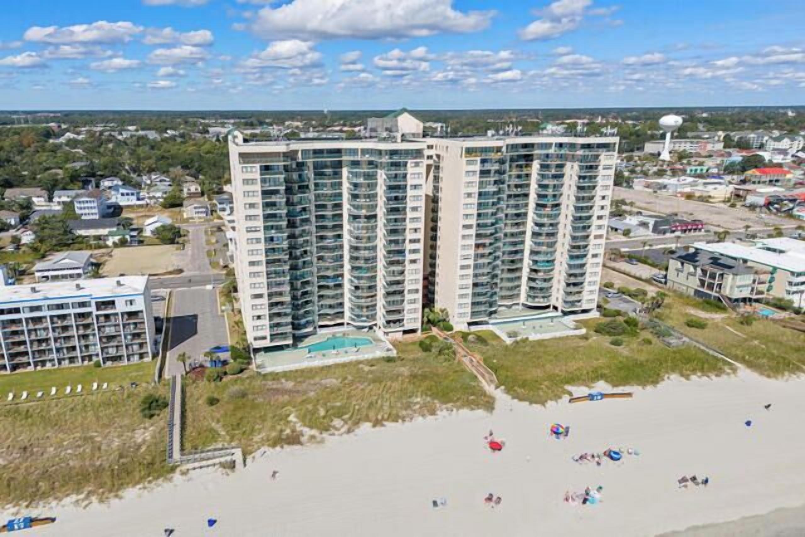 A high-rise hotel with multiple balconies, a pool, and a beach view.