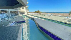 A pool area with a clear view of the ocean, a covered seating area, and a lifeguard stand.