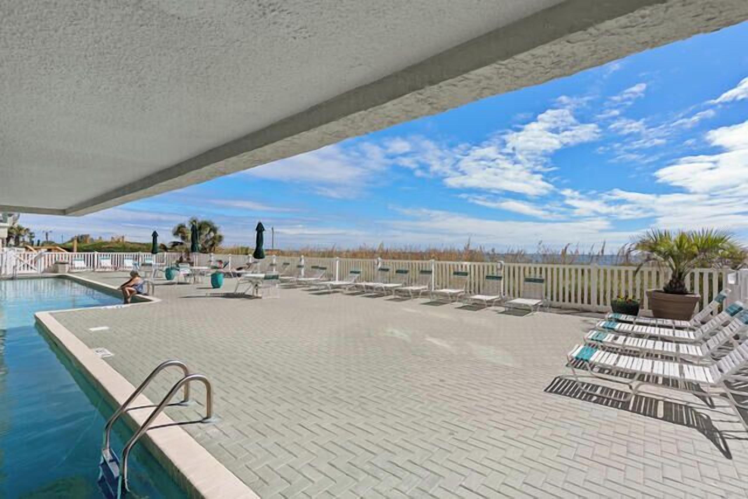 A pool area with lounge chairs and a view of the beach.