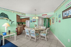 A dining area with a round glass table and wicker chairs, a kitchen with wooden cabinets, and a fish mural on the wall.