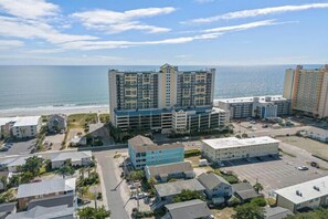 A high-rise hotel with multiple floors, a parking lot, and a view of the ocean.