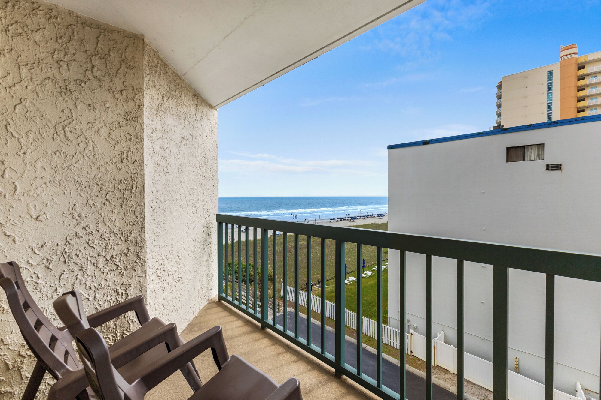 A balcony with a view of the ocean and a white building with a blue roof.
