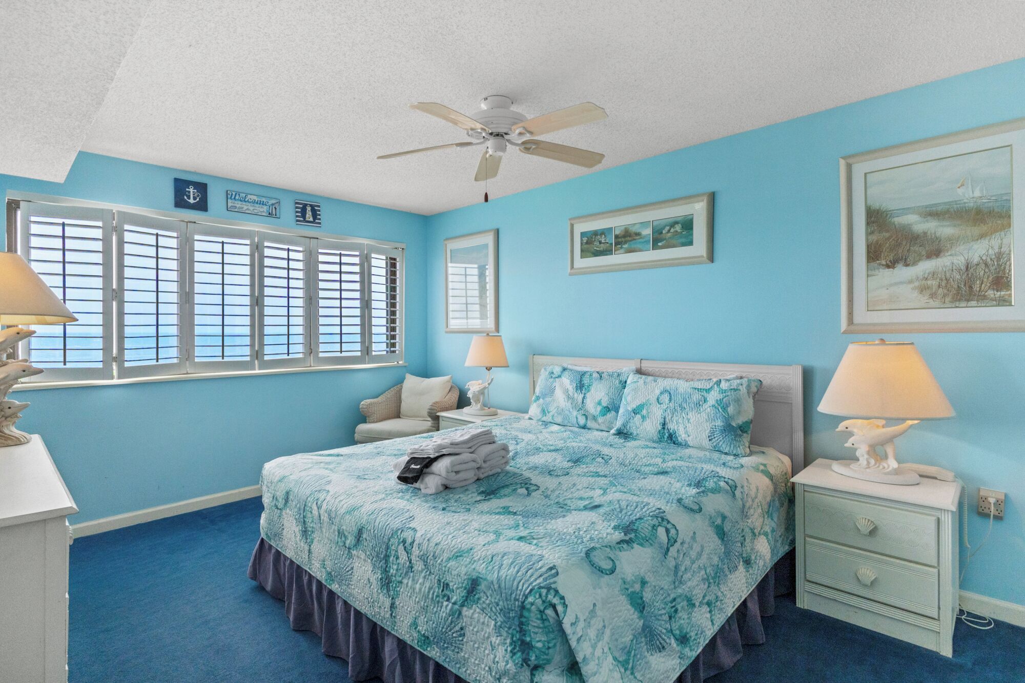 A bedroom with a bed, two nightstands, a ceiling fan, and a window with shutters.