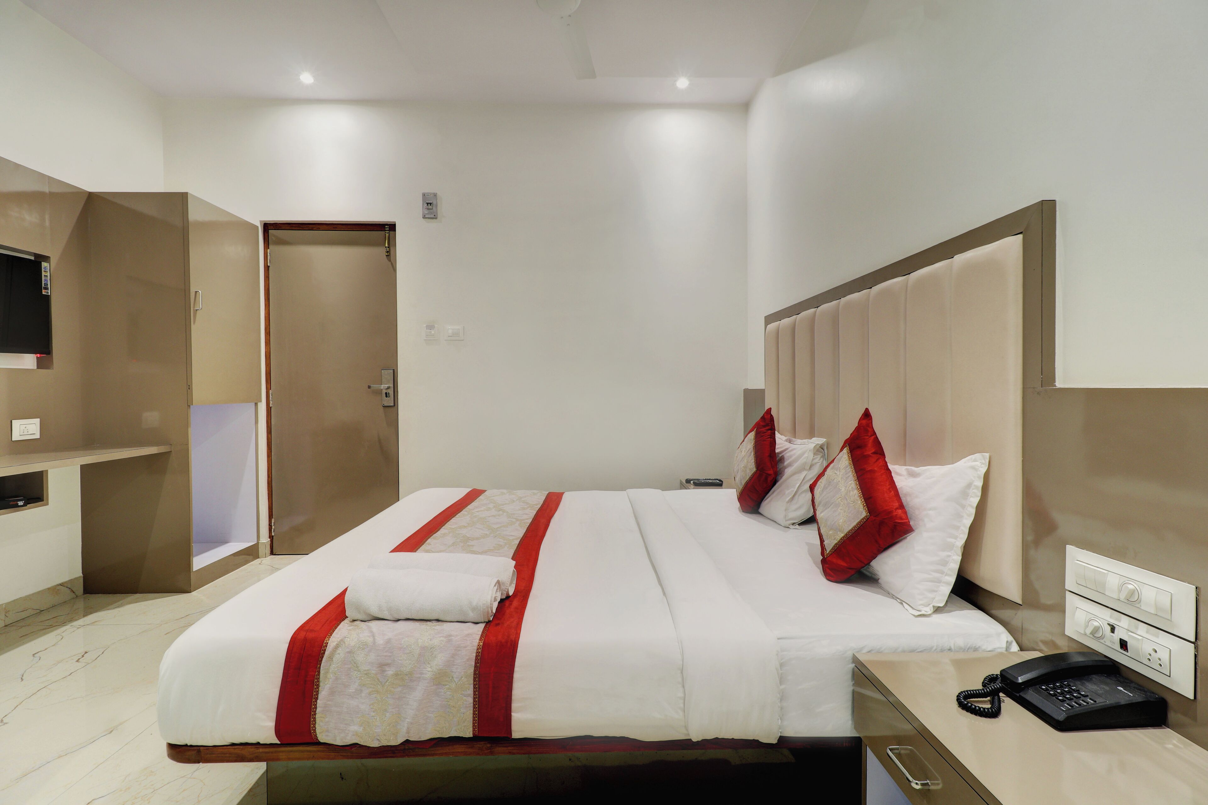A hotel room with a bed, a bedside table with a phone, and a TV mounted on the wall.