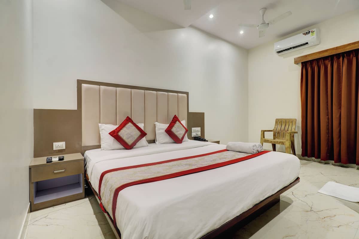 A hotel room with a large bed, a wooden nightstand, a chair, and an air conditioning unit.