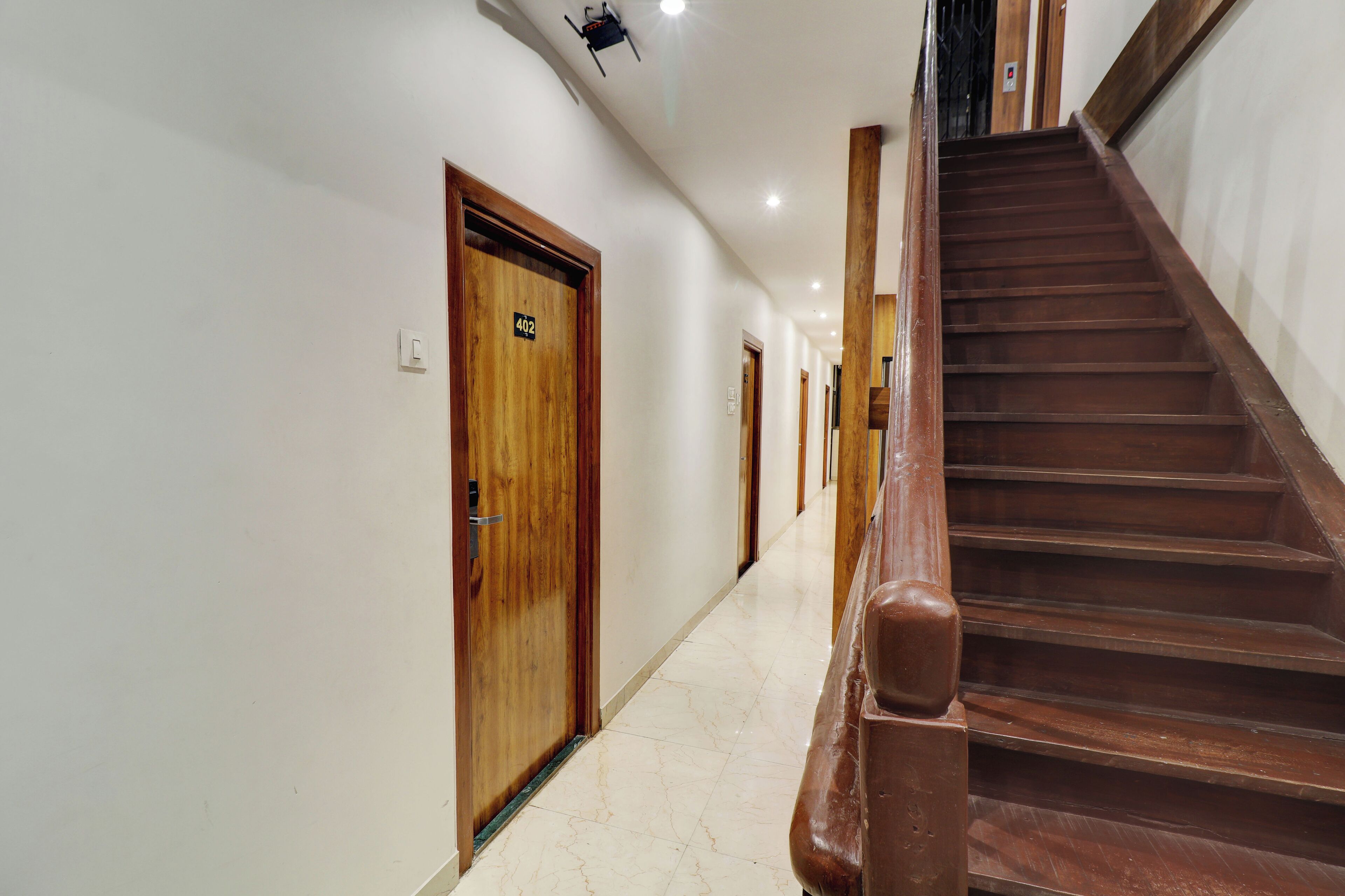 A hotel hallway with wooden doors, a marble floor, and a wooden staircase.