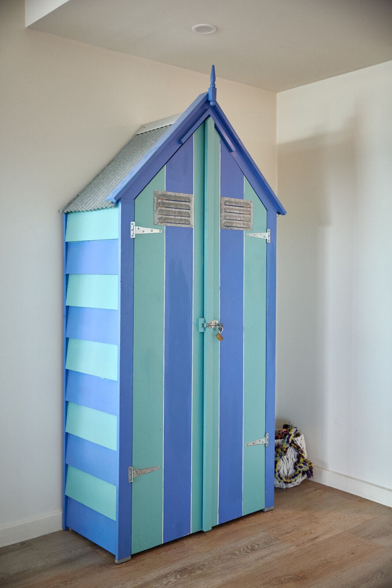 Een kamer met een grote, gestreepte kast in blauw en turquoise, een houten vloer en een witte muur.