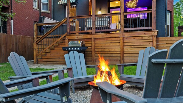 Una terraza con sillas Adirondack, una fogata y un edificio con zona de bar al fondo.