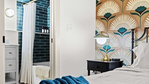 Un dormitorio con cama, mesita de noche con lámpara, ventana con cortina y pared con estampado floral.