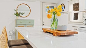 Una cocina moderna con una isla grande, un espejo redondo, un jarrón con flores amarillas y una tabla de madera para servir.