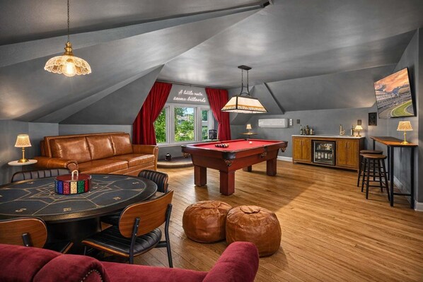 Una habitación estilo loft acogedora con mesa de billar, sofá de cuero y zona de comedor.