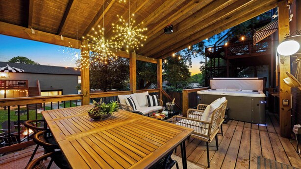 Una terraza al aire libre con una mesa y sillas de madera, un jacuzzi y luces colgantes.