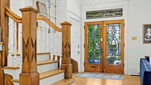 Una escalera con balaustres y barandilla de madera que conduce a una puerta doble con paneles de vidrio emplomado.