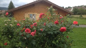 A wooden cabin with a visible door and windows, surrounded by a garden with blooming roses. - Detached chalet on a farm in the Jura (Lent)
