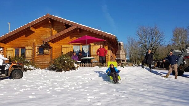 A wooden cabin with a red umbrella, snow-covered ground, and a person in a wheelchair. - Detached chalet on a farm in the Jura (Lent)