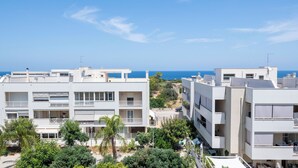 A modern apartment complex with multiple balconies, a view of the sea, and surrounding greenery.