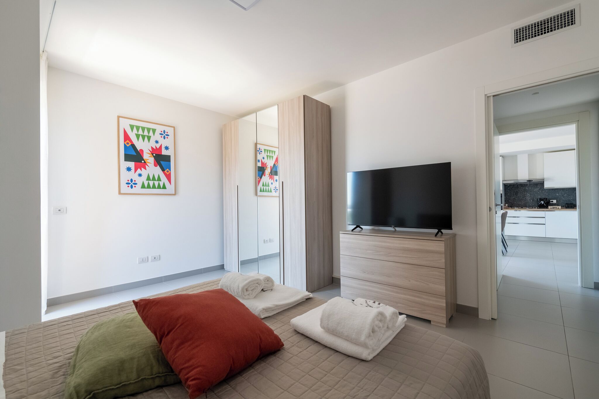 Une chambre d’hôtel moderne équipée d’un lit, d’une télévision, d’une armoire et d’une salle de bain visible à travers une porte ouverte.