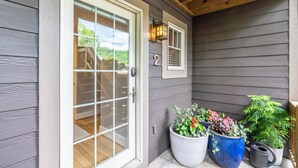 A house entrance with a sliding glass door, a small porch with wooden beams, and potted plants.