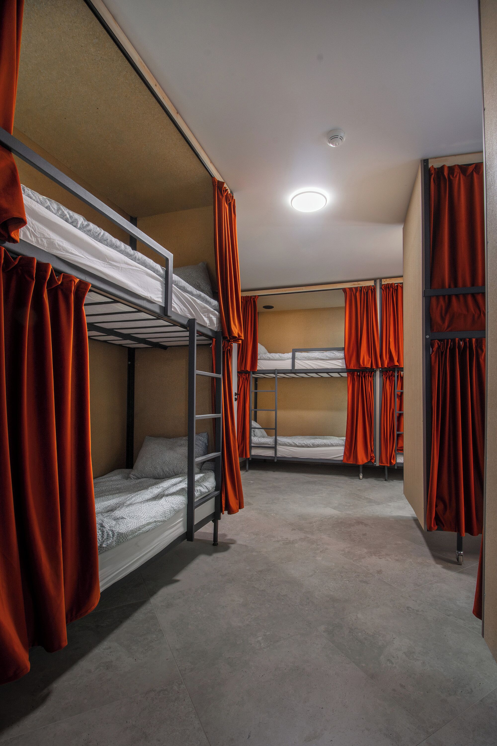 Ein Schlafsaalzimmer mit Etagenbetten, orangefarbenen Vorhängen und einer Deckenleuchte.