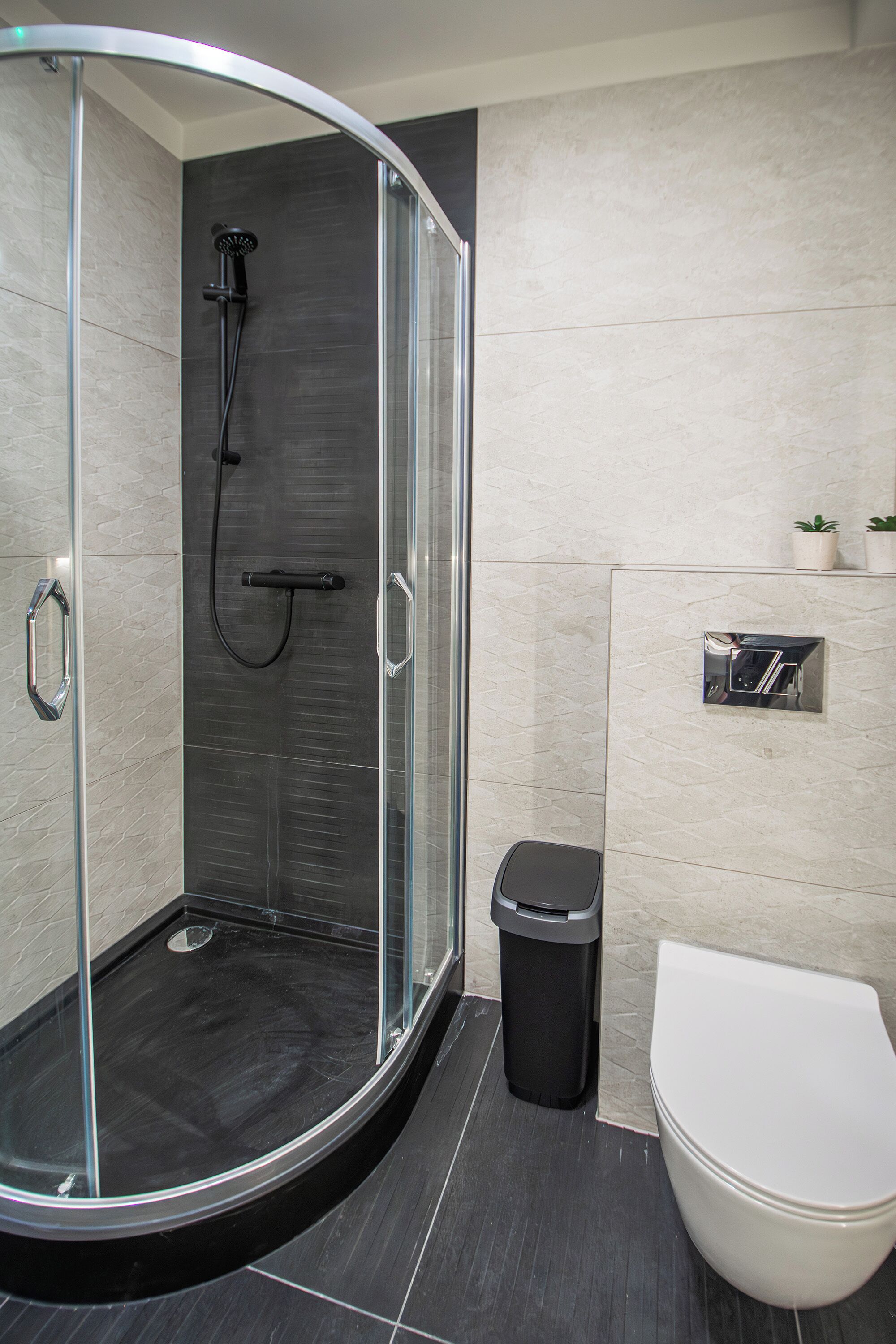 Un baño moderno con ducha envuelta en vidrio, un inodoro blanco y un cubo de basura.