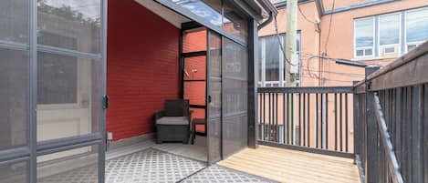 Un balcon avec un mur rouge, une chaise en osier et une terrasse en bois.