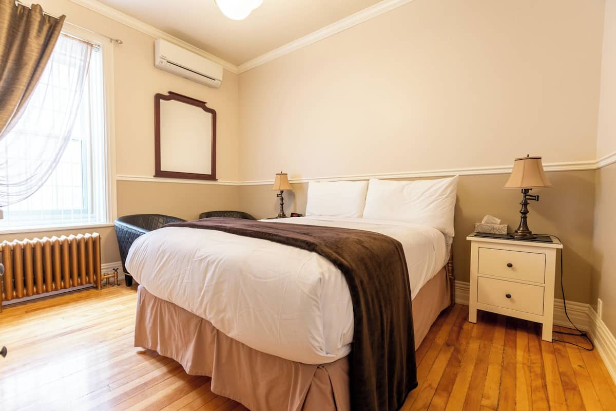 A hotel room with a bed, bedside tables, a radiator, and a window with curtains.