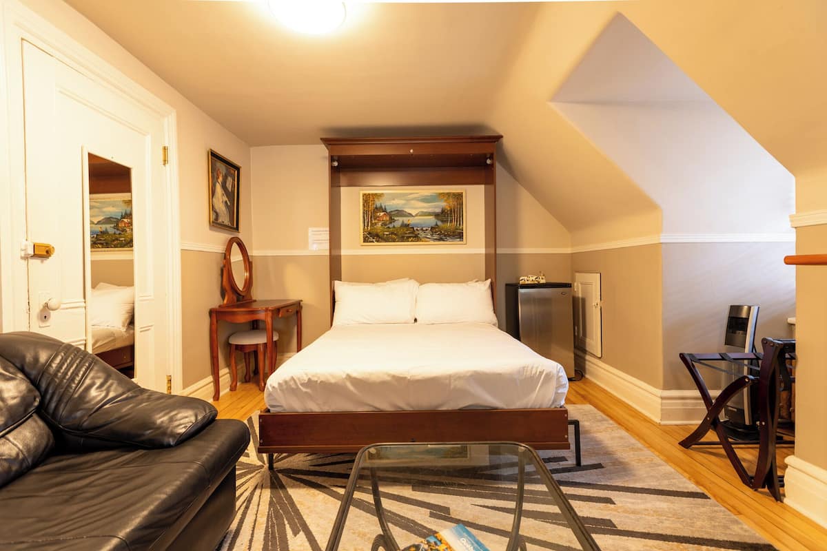 A bedroom with a bed, a desk, a chair, a mirror, and a painting on the wall.