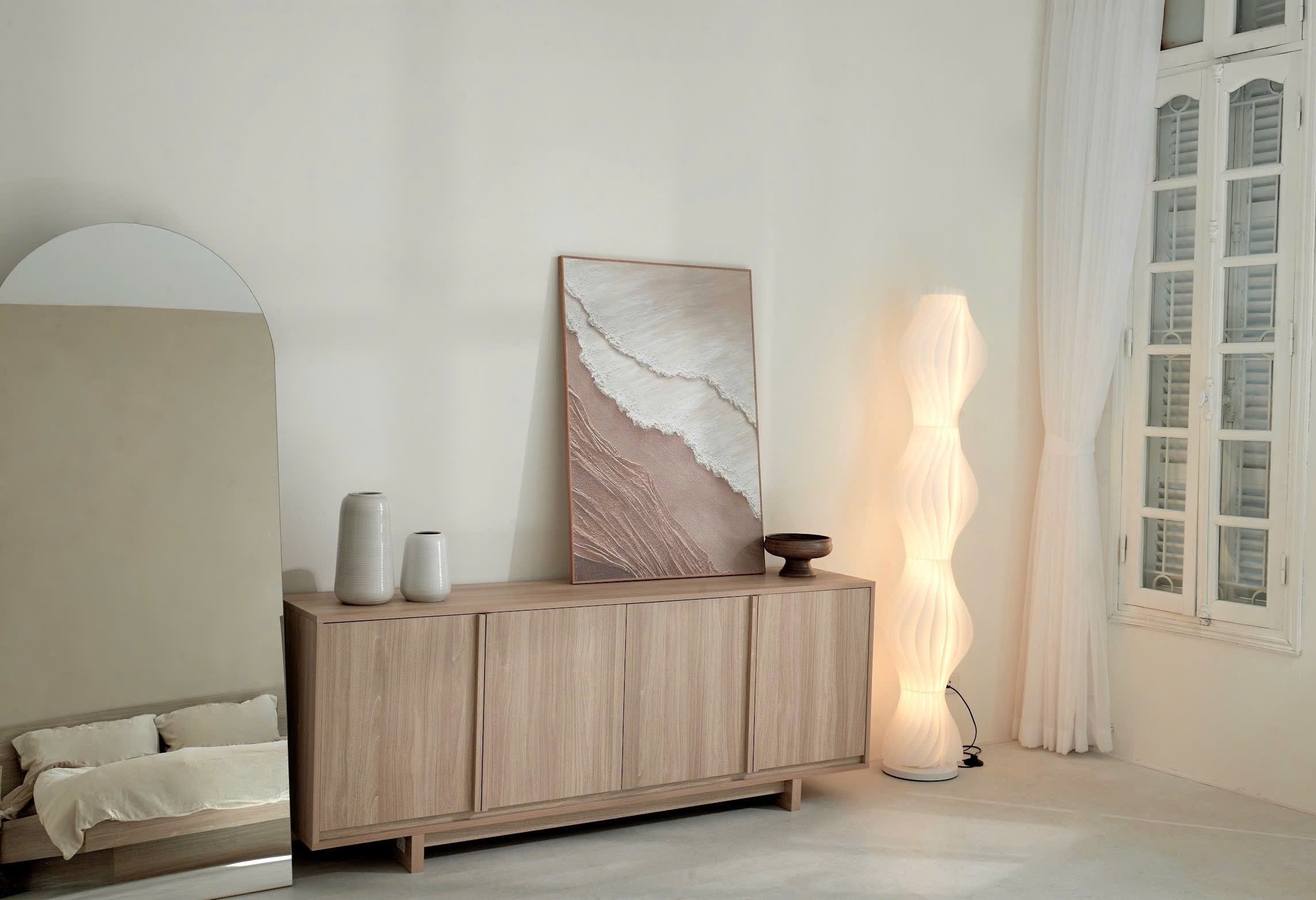 Une chambre à coucher au style minimaliste, avec un lit, une commode en bois agrémentée d’objets décoratifs, un tableau et un grand lampadaire au pied texturé.