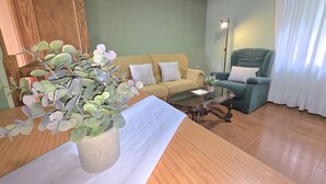 A living room with a wooden coffee table, a beige sofa, a green armchair, and a potted plant. - Lidya's House - 36801 (Entrambasaguas)