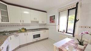 A kitchen with white cabinets, a built-in oven, a washing machine, and a dining area with a table and chairs. - Lidya's House - 36801 (Entrambasaguas)