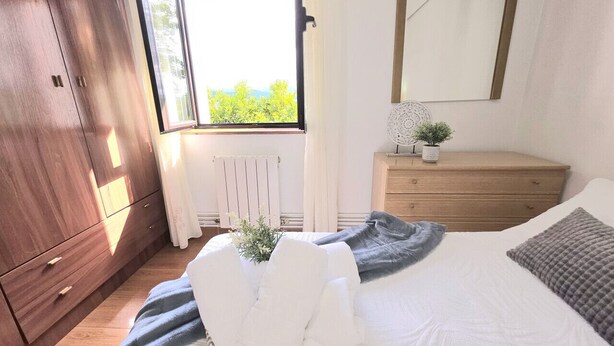 A bedroom with a bed, a dresser, a mirror, and a window with a view of greenery. - Lidya's House - 36801 (Entrambasaguas)