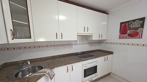 A kitchen with white cabinets, a granite countertop, a stainless steel sink, and a red coffee-themed wall decoration. - Lidya's House - 36801 (Entrambasaguas)