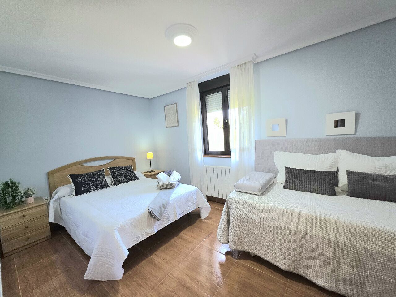 Une chambre avec deux lits, une table de chevet, une lampe et une fenêtre avec des rideaux.