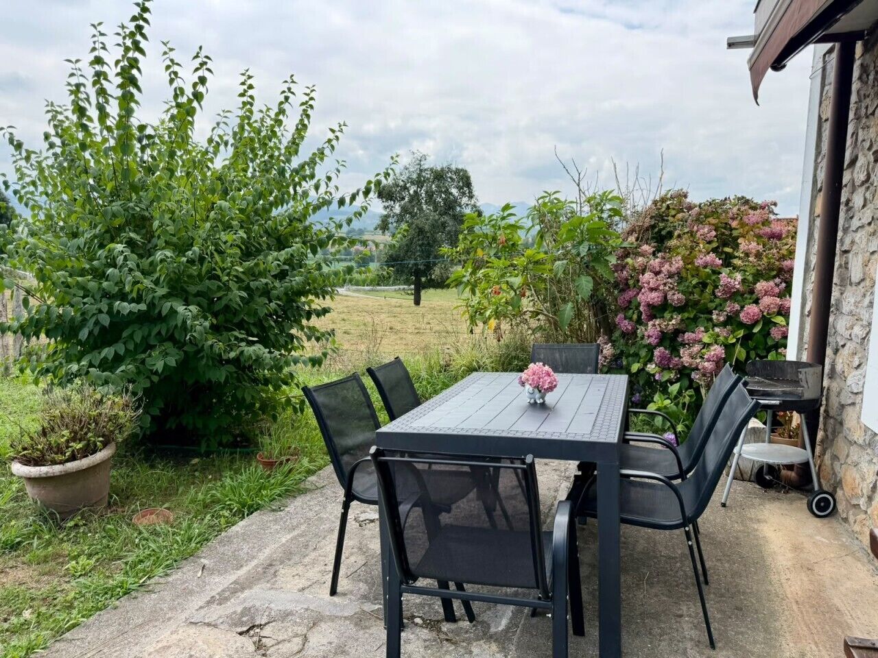 Une terrasse extérieure avec une table et des chaises, entourée de verdure et d’un mur en pierre.