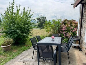 Un patio al aire libre con una mesa y sillas, rodeado de vegetación y un muro de piedra.