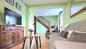 Un salon comprenant un canapé, un téléviseur, un meuble en bois et un escalier menant à une autre pièce.