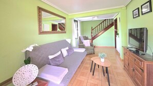Un salon comprenant un canapé, des fauteuils, une petite table, un téléviseur et un escalier menant à une autre pièce.