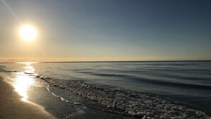 A beach scene with the sun low on the horizon, reflecting on the water. - Townhouse in Elviria with pool, Wi-Fi, barbecue and private terrace (Marbella)