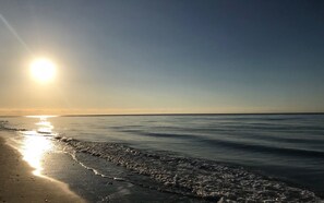 A beach scene with the sun low on the horizon, reflecting on the water. - Townhouse in Elviria with pool, Wi-Fi, barbecue and private terrace (Marbella)