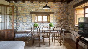 A rustic stone-walled room with a wooden ceiling, a table with chairs, and a hanging light fixture.
