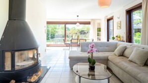 A modern living room with a large fireplace, a sofa, a glass coffee table, and a view of the outdoors.