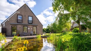 A modern house with a sloped roof, large windows, and a pond in the garden.